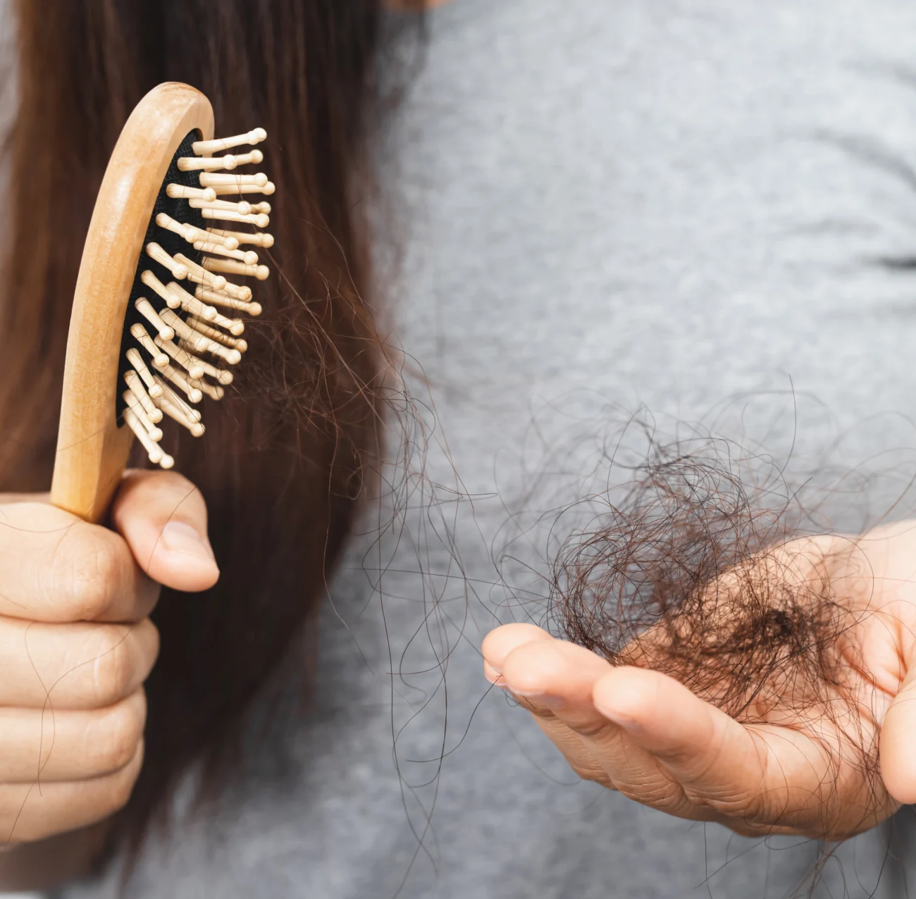A woman holding a hairbrush and a handful of shed hair